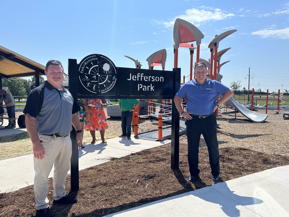 Two men stand in front of a sign for a park