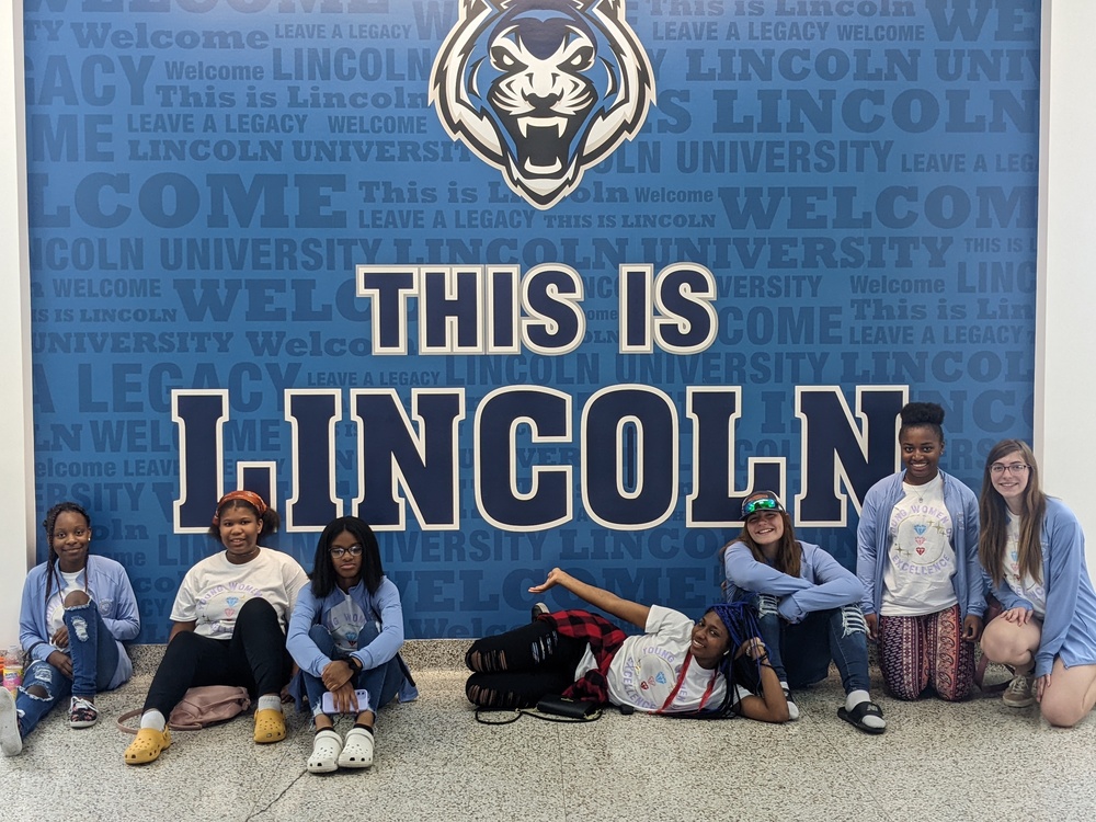 A group of female students pose in front of a sign that reads "This is Lincoln" at Lincoln University.