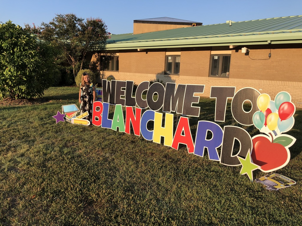 A student stands smiling beside a sign that says Welcome to Blanchard