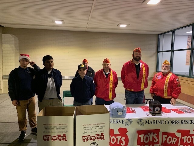 Cadets pose with other workers at the Marine Reserves Toys-4-Tots table and drop-off boxes