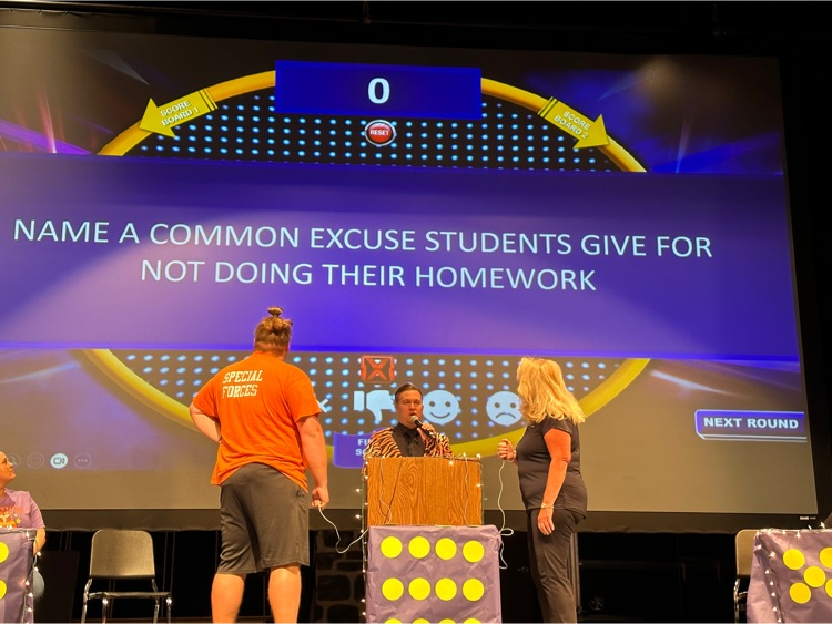 two people stand on stage competing in a game with an announcer behind a podium