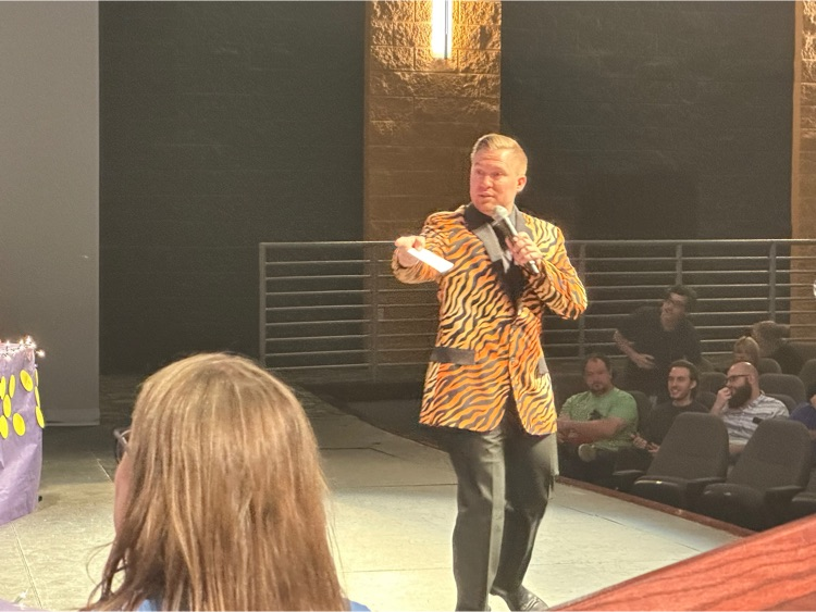 a game show host wears a Tiger blazer and points at contestants