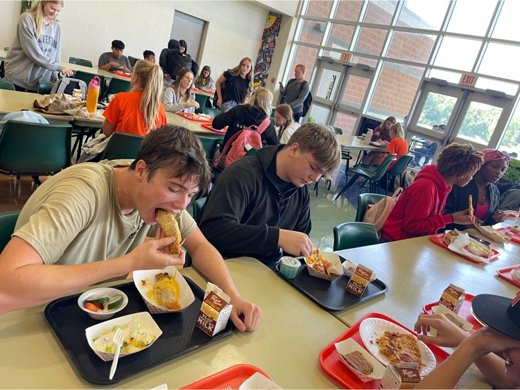 a boy eats a crispito at the lunch table with his friends