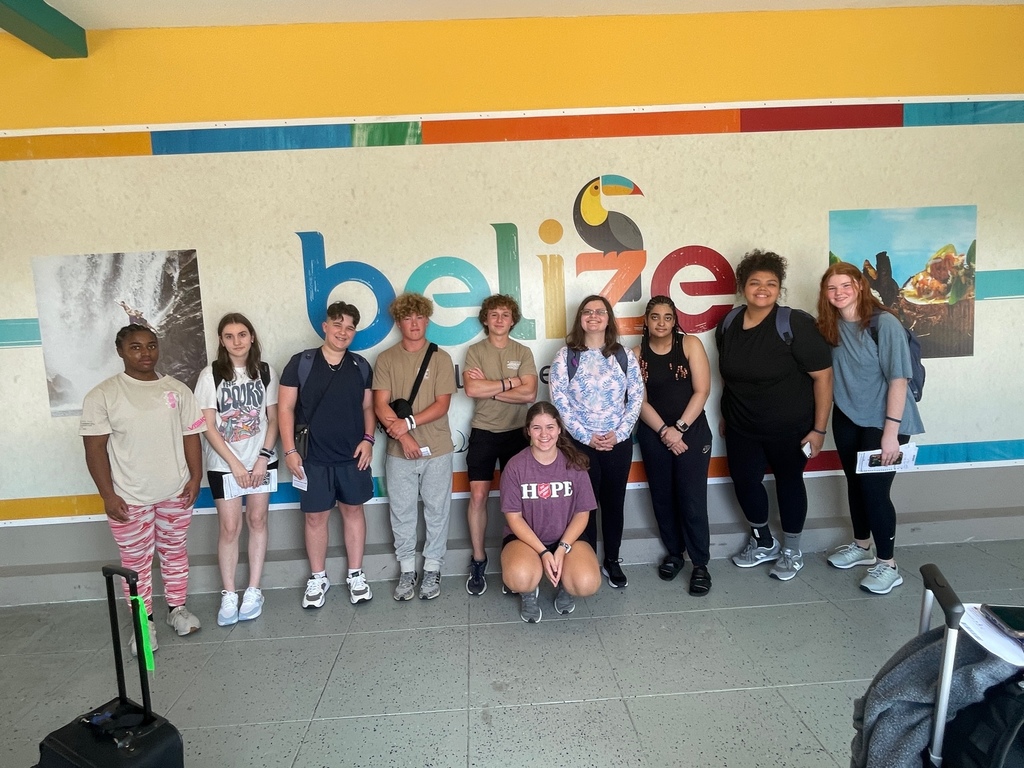 A group of young people stand in front of a sign that says "Belize" on it